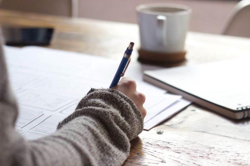 Woman writing in journal with coffee & laptop nearby
