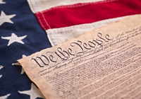 Photo of the american flag and a portion of the first page of the U.S. Constitution