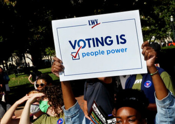 crowd marching black woman holding sign that reads voting is people power