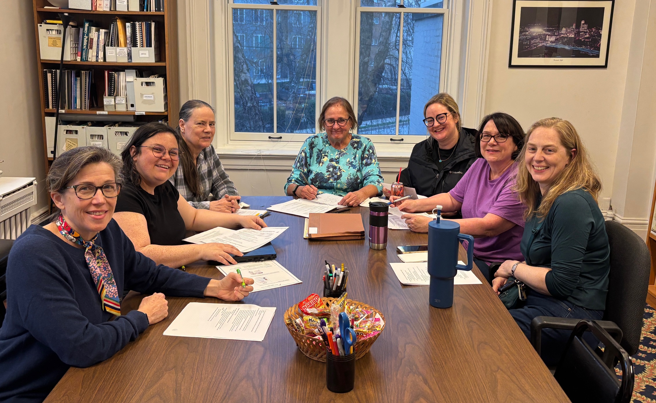 A group of women at a table with paperwork, smiling at camera
