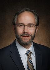 Man with a beard, wearing glasses and suit