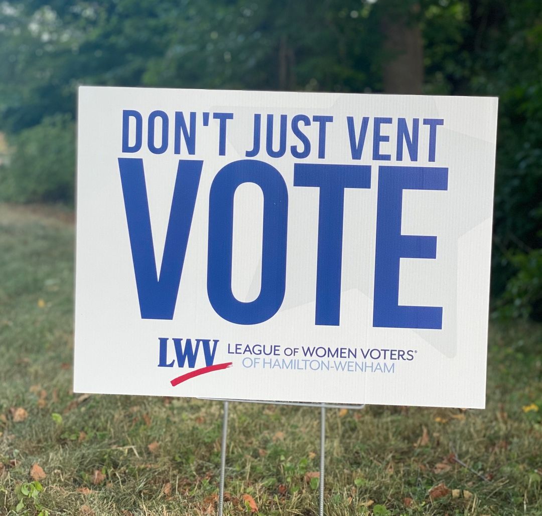 White lawn sign with League of Women Voters logo and blue text reading Don't just vent, VOTE!