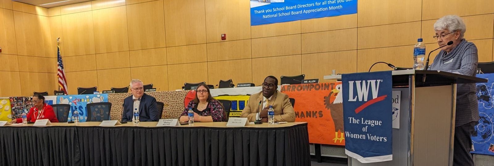 Candidates sitting at table with moderator standing at right