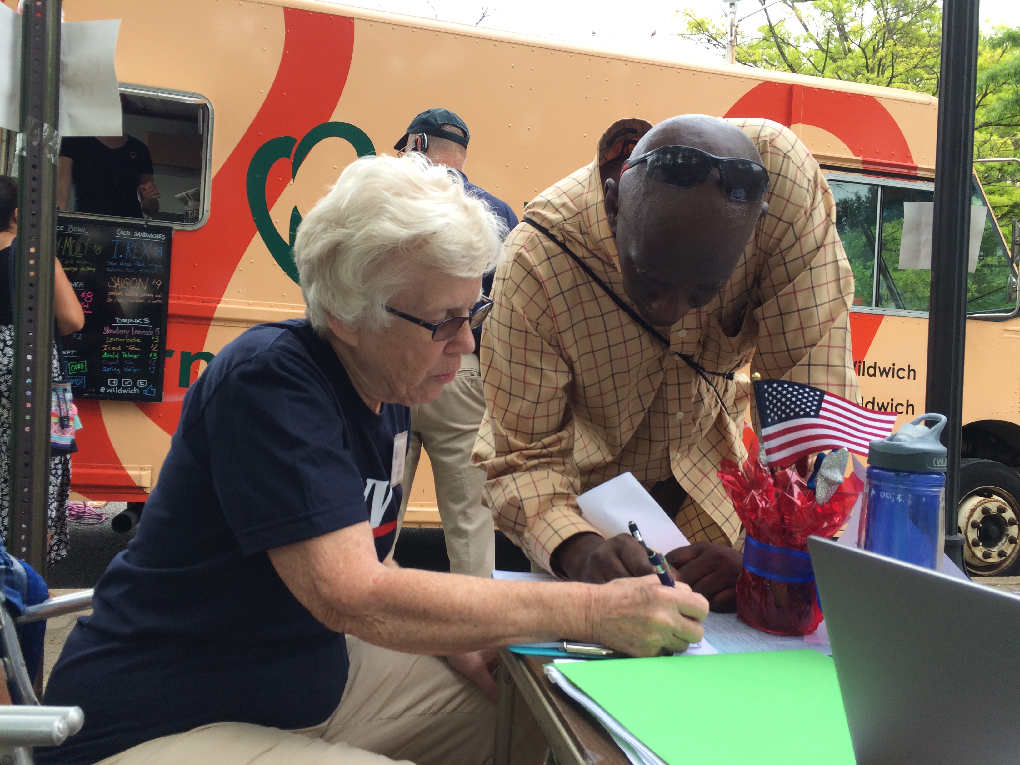 A League member helps a voter at a folding table outdoors in front of a food truck 