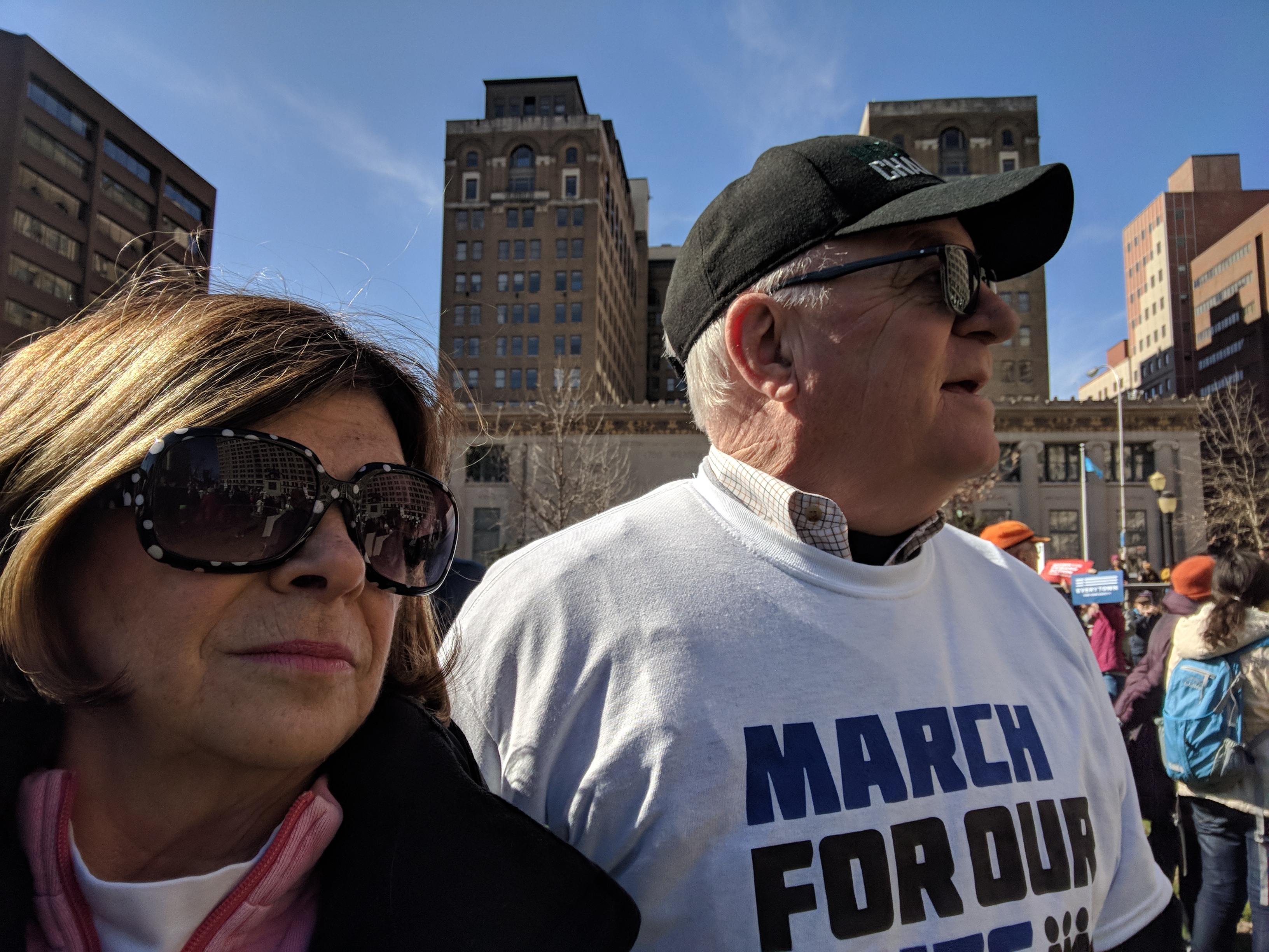 Woman and man standing outdoors in city, man wearing "March for our..." t-shirt