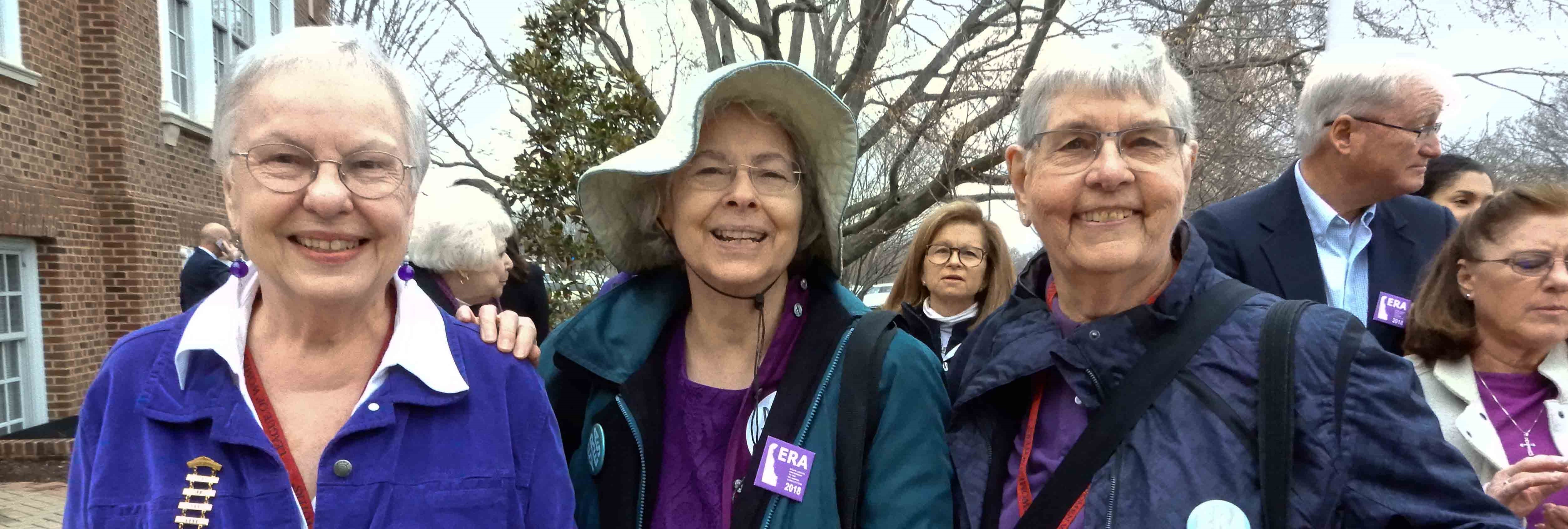 Women and men wearing purple; central woman also wearing "Delaware ERA 2018" button