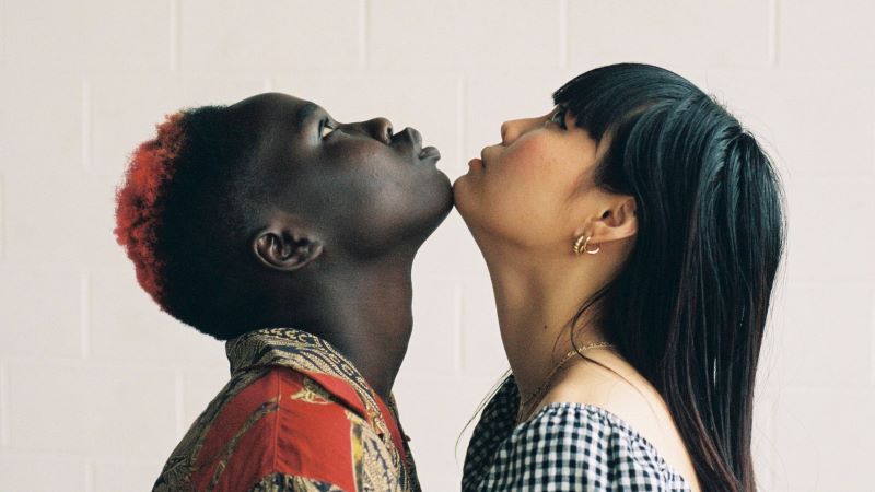 Photo of two people, one black and one asian looking up and touching chins