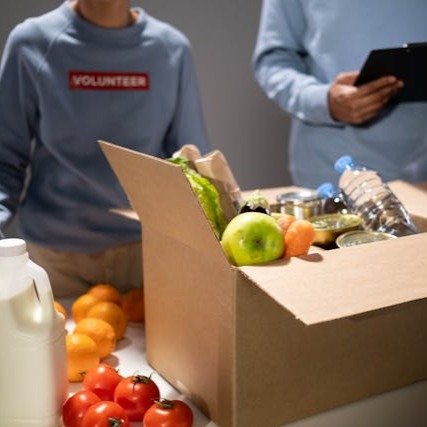 a box of groceries in the foreground is being filled by volunteers