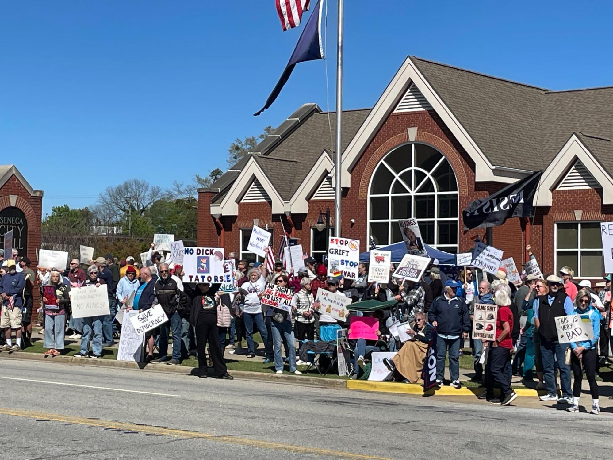 A large group of people in front of a building. They are waving protest signs.