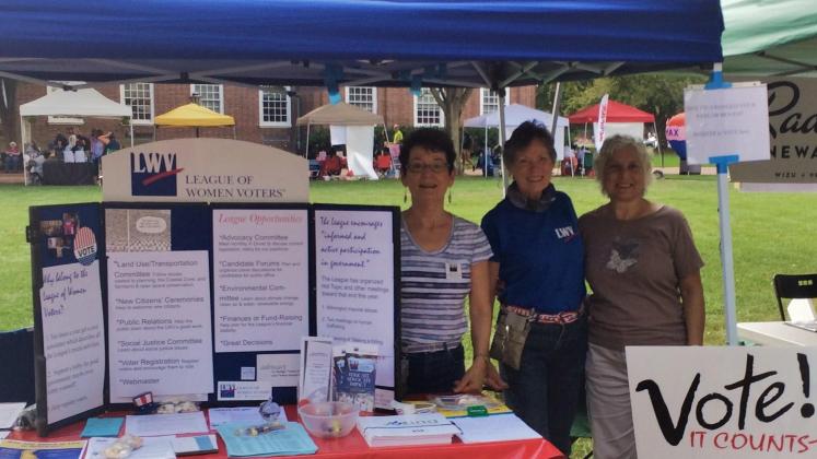 three women standing behind a League voter information table 