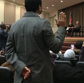 Man taking oath is shown from behind with his right hand raised 