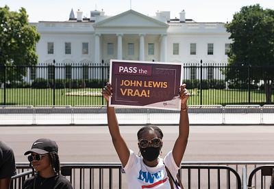 black woman standing in front of the white house holding a sign that reads  Pass the John Lewis Voting Rights Act Amendment