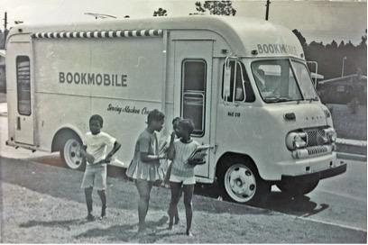 Black and white photo of bookmobile with 3 children in front