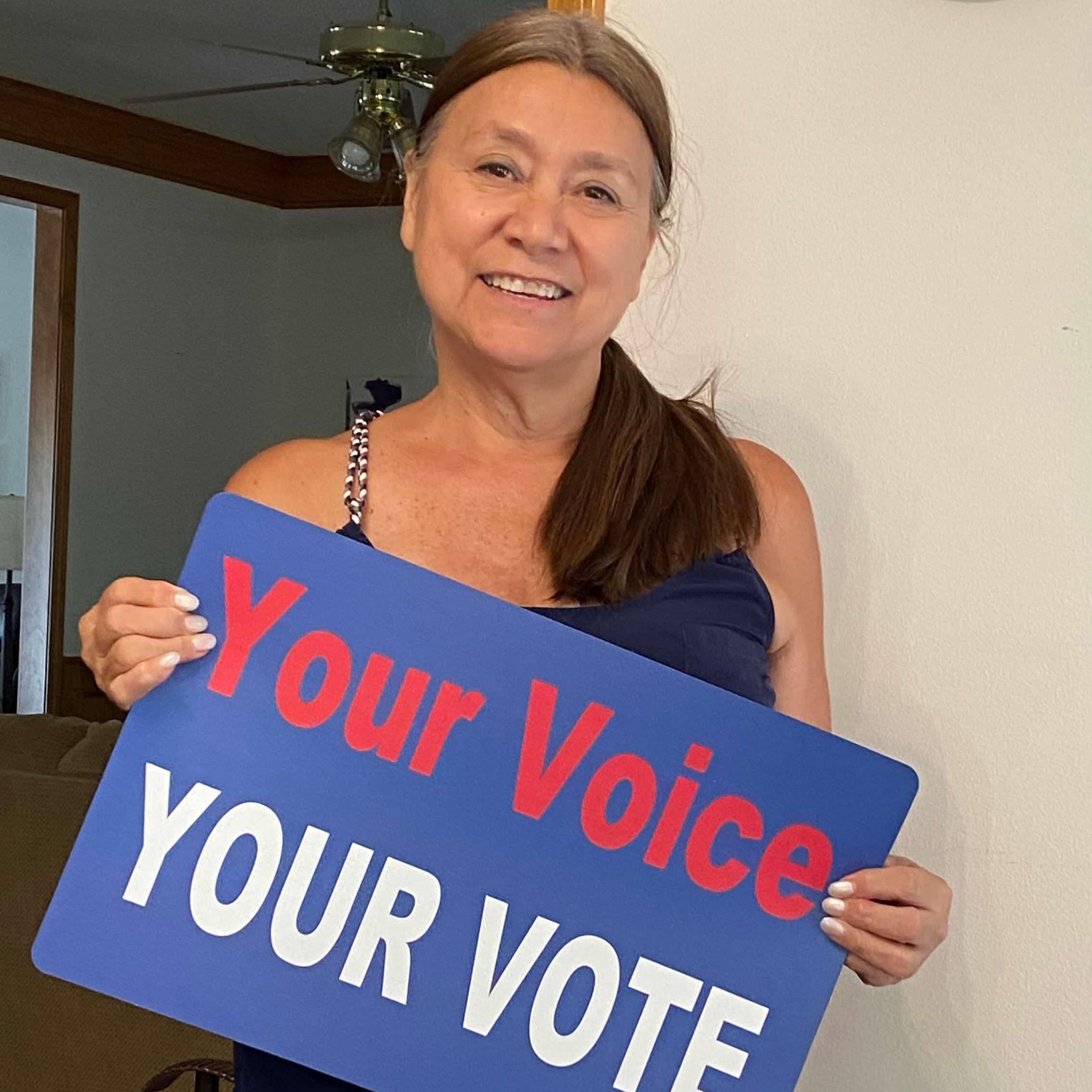 Woman with long dark ponytail holding a Your Voice Your Vote sign