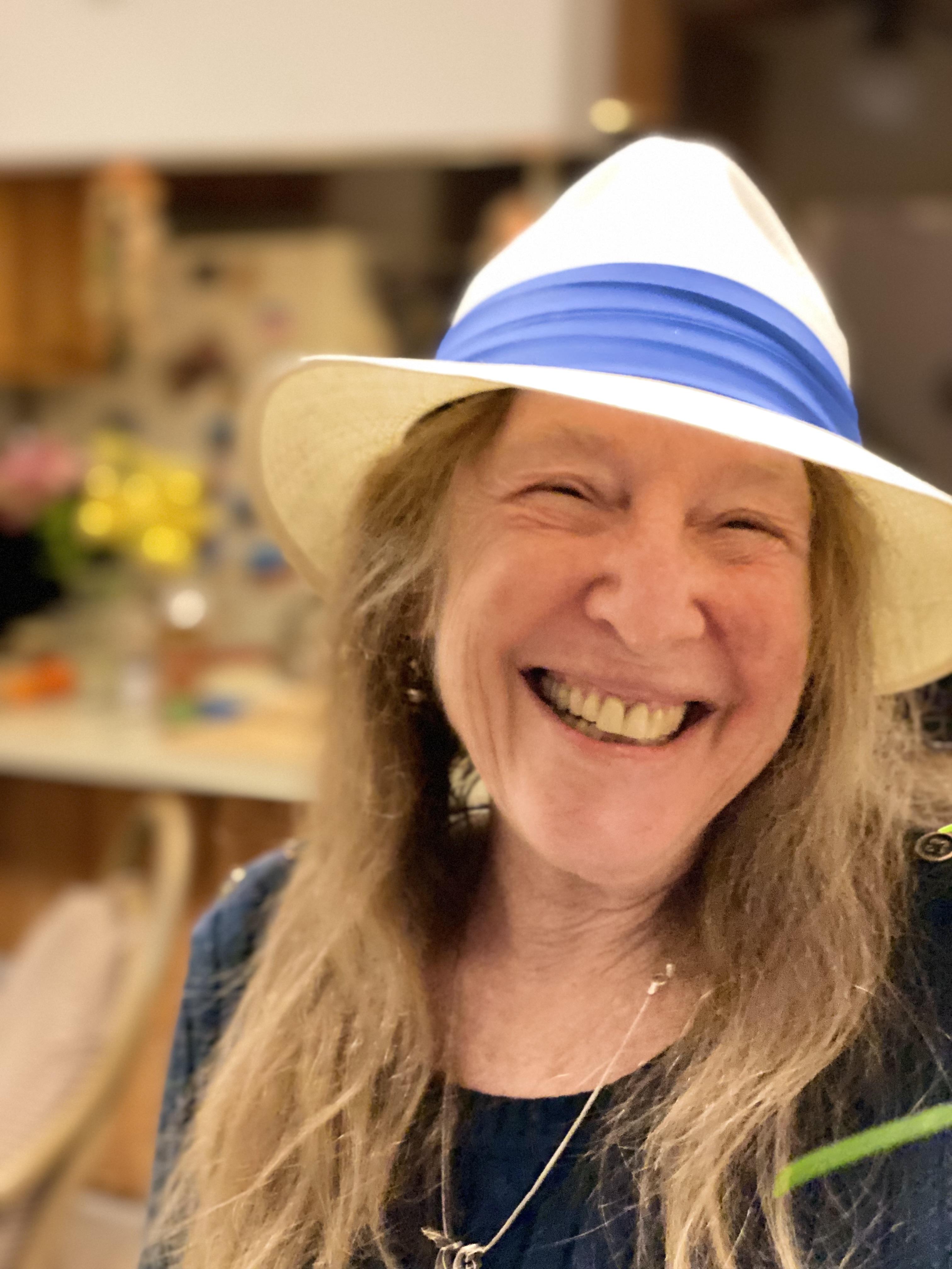 Smiling woman with long blonde/brown hair and straw hat with blue band