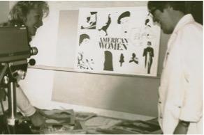 Sepia photo of woman and man looking over table of historical documents with camera in foreground