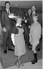 Black and white photo three gentlemen in back with model airplane and two women in front