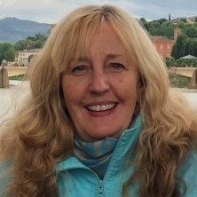 Head shot of white woman with long thick blonde hair wearing an aqua jacket