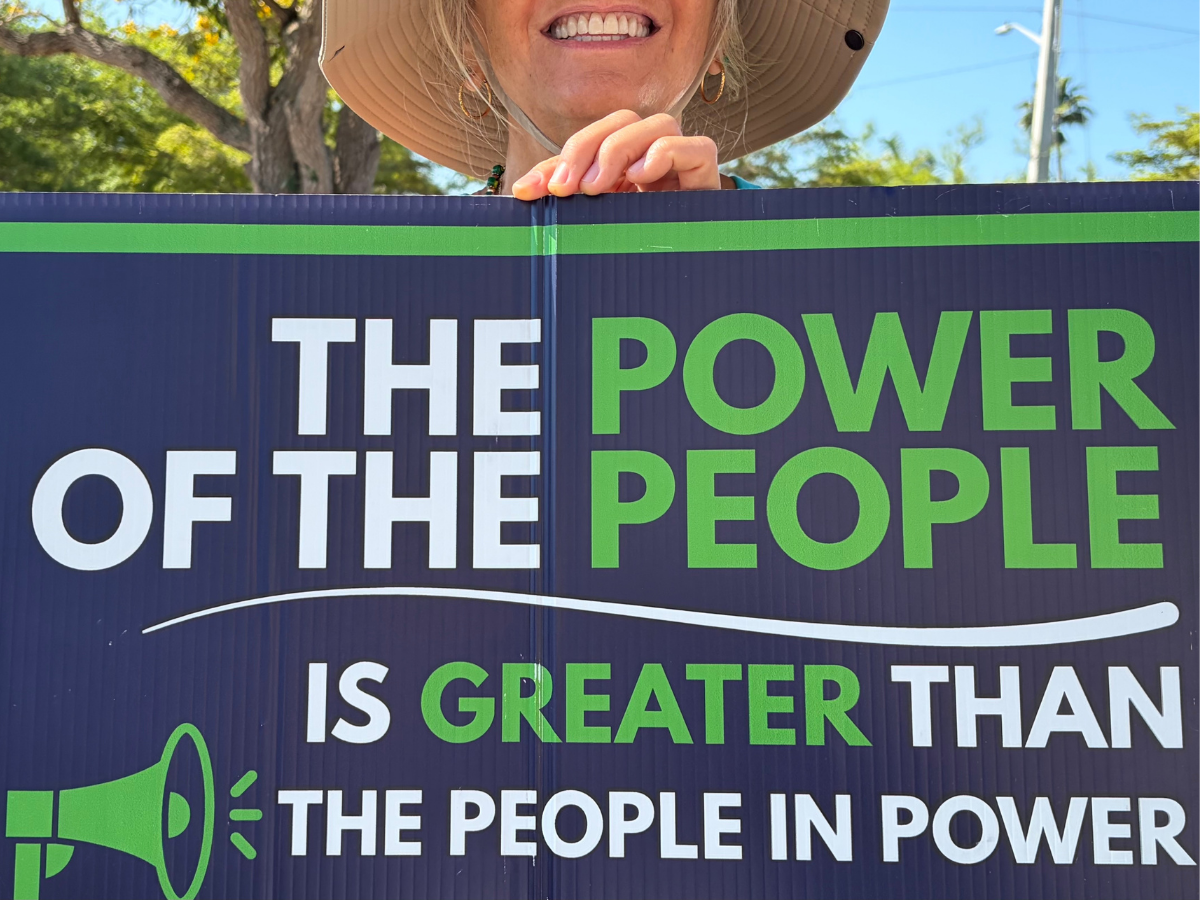 The Power of the People Smiling person holding sign that says "the power of the people is greater than the people in power"