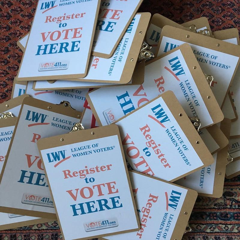 a pile of LWV clipboards with Register to VOTE HERE, the LWV logo, and Vote411