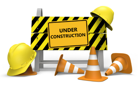Under Construction sign on barrier with traffic cones and hard hats