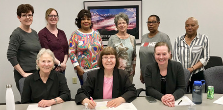 Two rows of women (one seated, one standing) smile at the camera