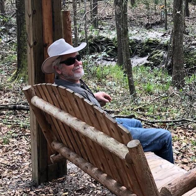 Gentleman with cowboy hat sitting in wooden swing seat with woods in the background