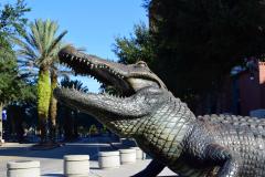 Close up of head of bronze alligator statue with palm trees in background