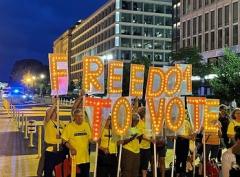 nighttime photo of people marching on a city street holding signs of letters that spell freedom to vote