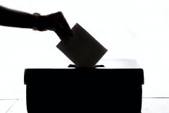 Hand in shadow dropping paper in ballot box