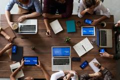 Individuals meeting around a table covered with laptops and tablets.