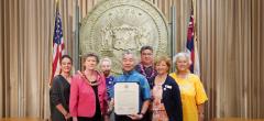 Hawaii State League of Women Voters members with Governor David Ige and proclamation in front of state seal and flags
