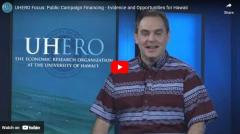 UHERO's Colin Moore in front of a screen with the UHERO logo facing the camera
