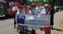 Photo of women at a parade holding signs and a banner that says Redding League of Women Voters