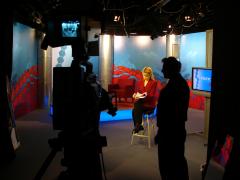 TV studio, cameramen in foreground with woman on stool in spotlight