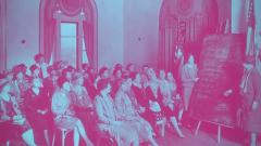 Historical image of women in a meeting looking at a list on a chalk board