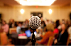 Microphone in foreground; blurred audience behind it.