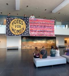 Picture of lobby where a flag reading votes for women is displayed