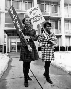 Two women in front of a building holding pro-voting signs
