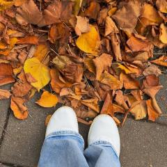 looking down at two feet near a pile of autumn leaves