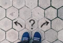 Person looking at the their feet trying to decide which way to go with a right arrow, left arrow and question mark in the middle