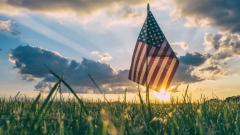 American Flag backlit by setting sun in field