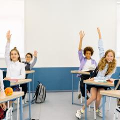 students sitting at desks with hands raised