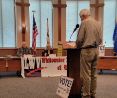 Candidates sit by microphones to answer questions, Moderator stands at podium asking questions