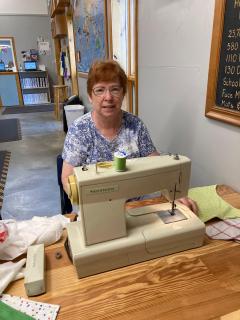 A picture of our Board Secretary, Midge Gill, at a sewing machine. 