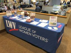 LWVNCC voter services table shown indoors with full table skirt and informational items spread out