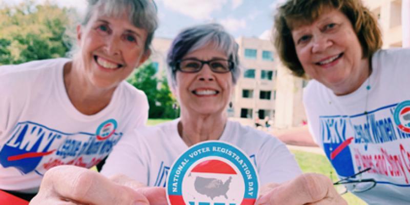 League members close-up, one extends arms holding National Voter Registration Day sticker