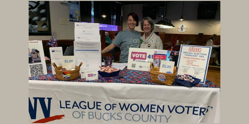 photo of 2 women, both white standing behind a voter registration and information table at the Bucks the System event in Levittown
