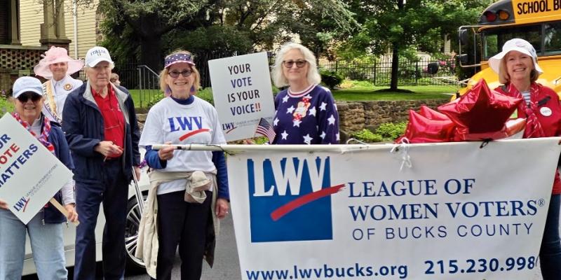 photo of women marching in parade holding a banner with league of women voters of bucks county