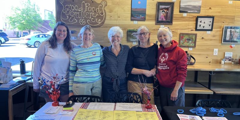 Four women stand behind a table that holds voter information.